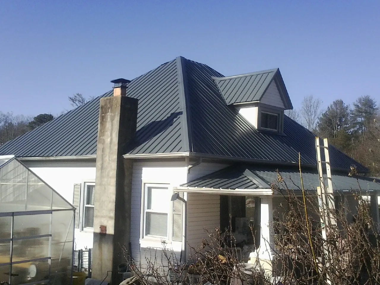 Dark blue standing seam metal roof on a white farmhouse with dormer — Slate & Tile Roof Repair by Roofing Brothers in Orrick