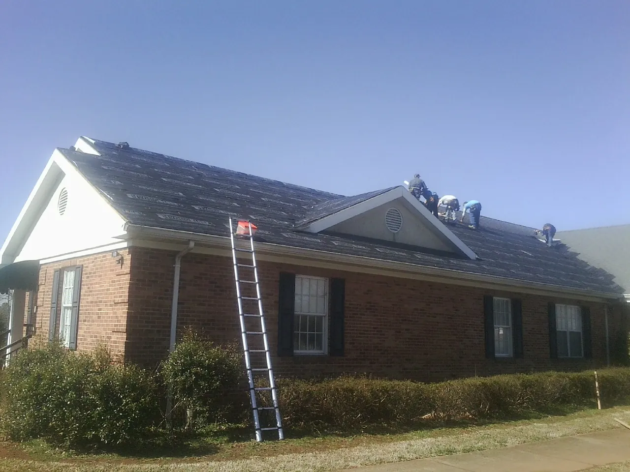 Crew tearing shingles off a brick ranch roof with a ladder set — Emergency Roof Repair work by our crew in Orrick