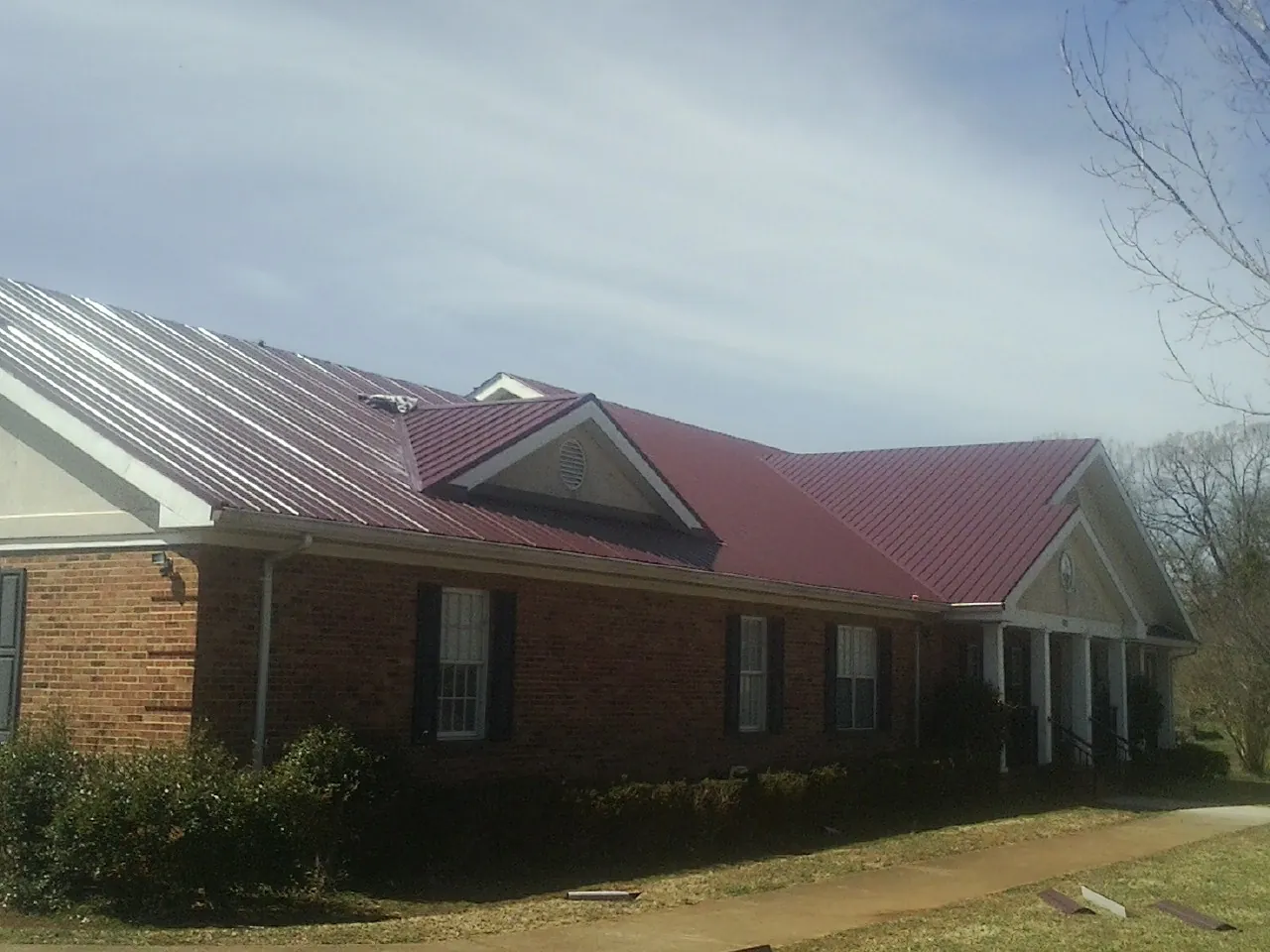 Red metal roof with gabled entries on a long brick building, from a Hail Damage Roof Repair job in Orrick