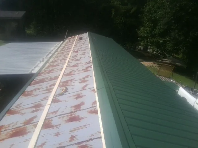 Old rusted panels beside newly installed green metal roofing — Wind Damage Roof Repair by Roofing Brothers in Orrick