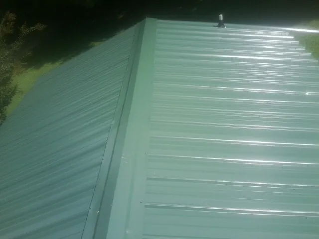 New green metal panels meeting at the ridge of a roof — Flat Roof Repair work by our crew in Orrick