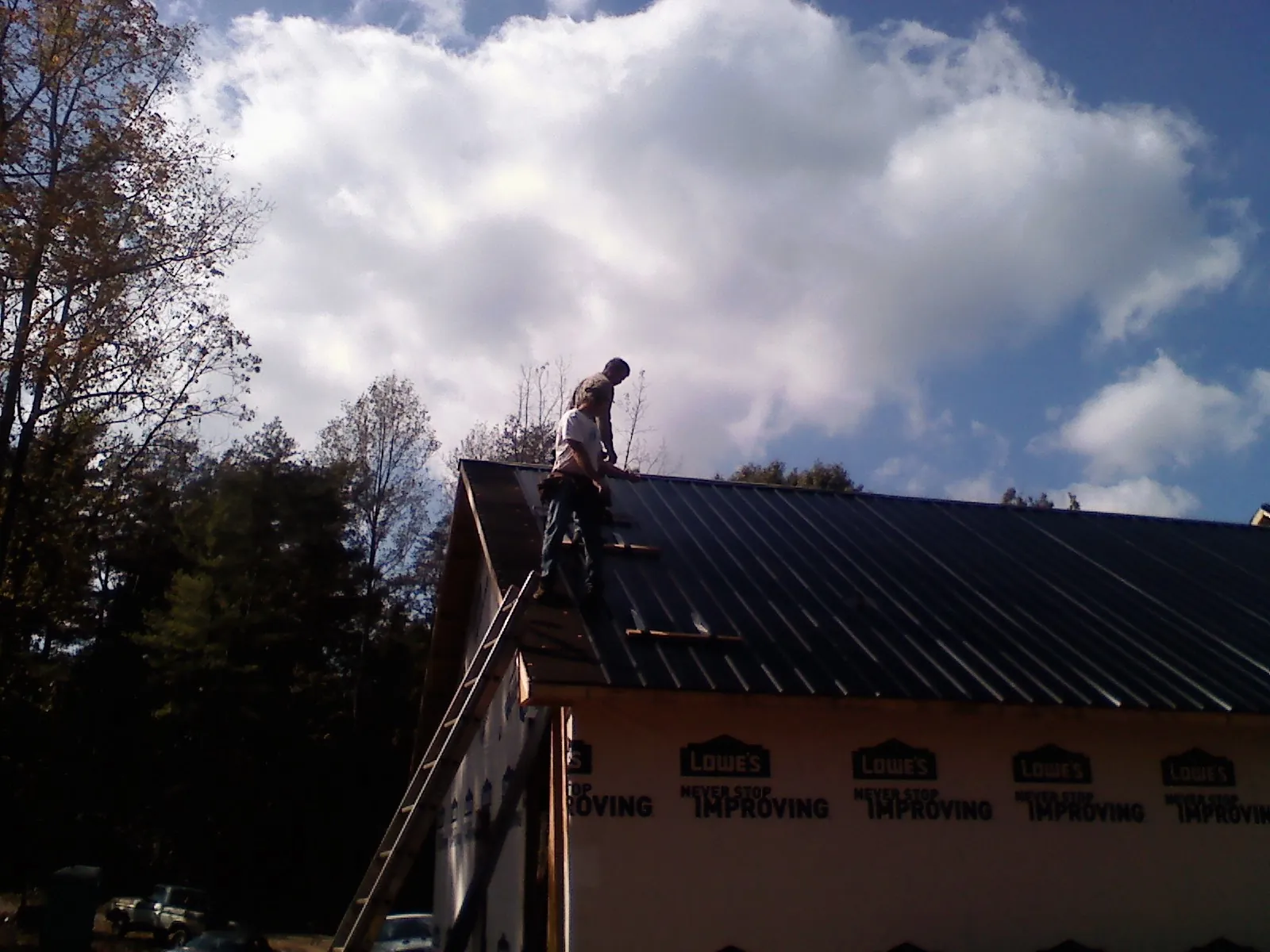 Roofer fastening dark metal panels high against a cloudy sky, from a Roof Inspection job in Orrick