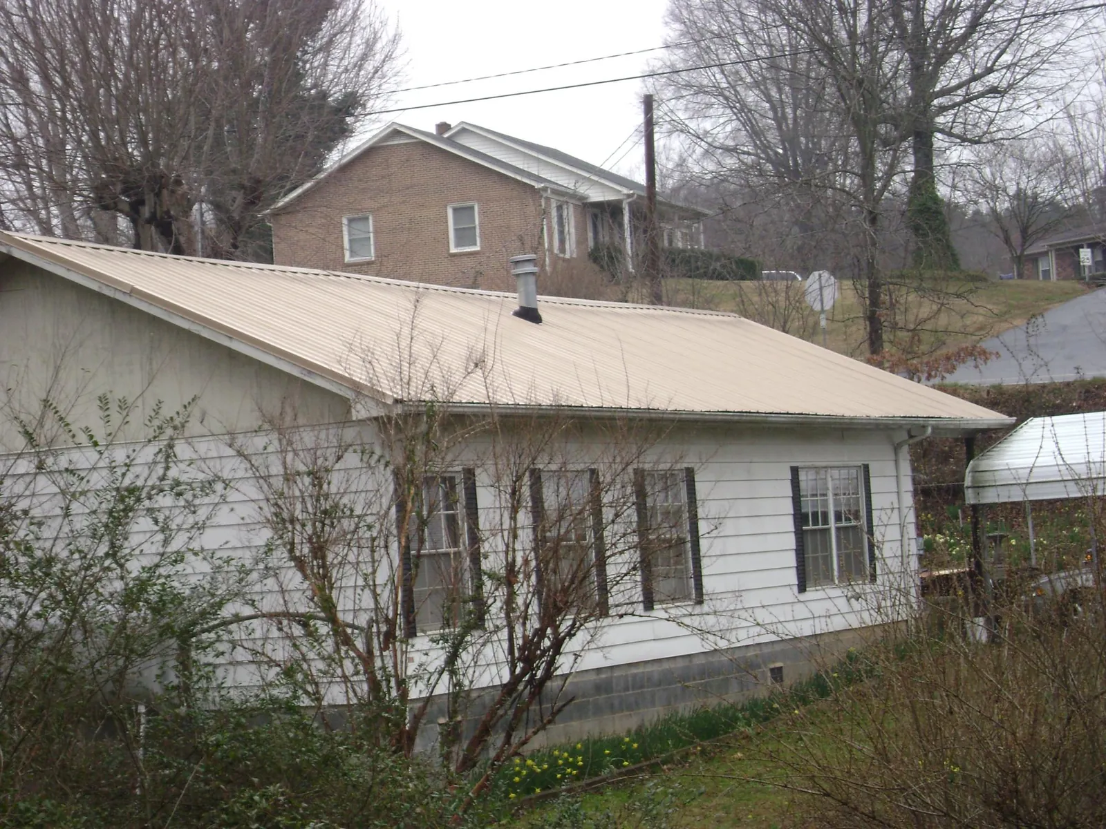 Tan metal roof on a white sided house set into a hillside — Commercial Roofing by Roofing Brothers in Orrick