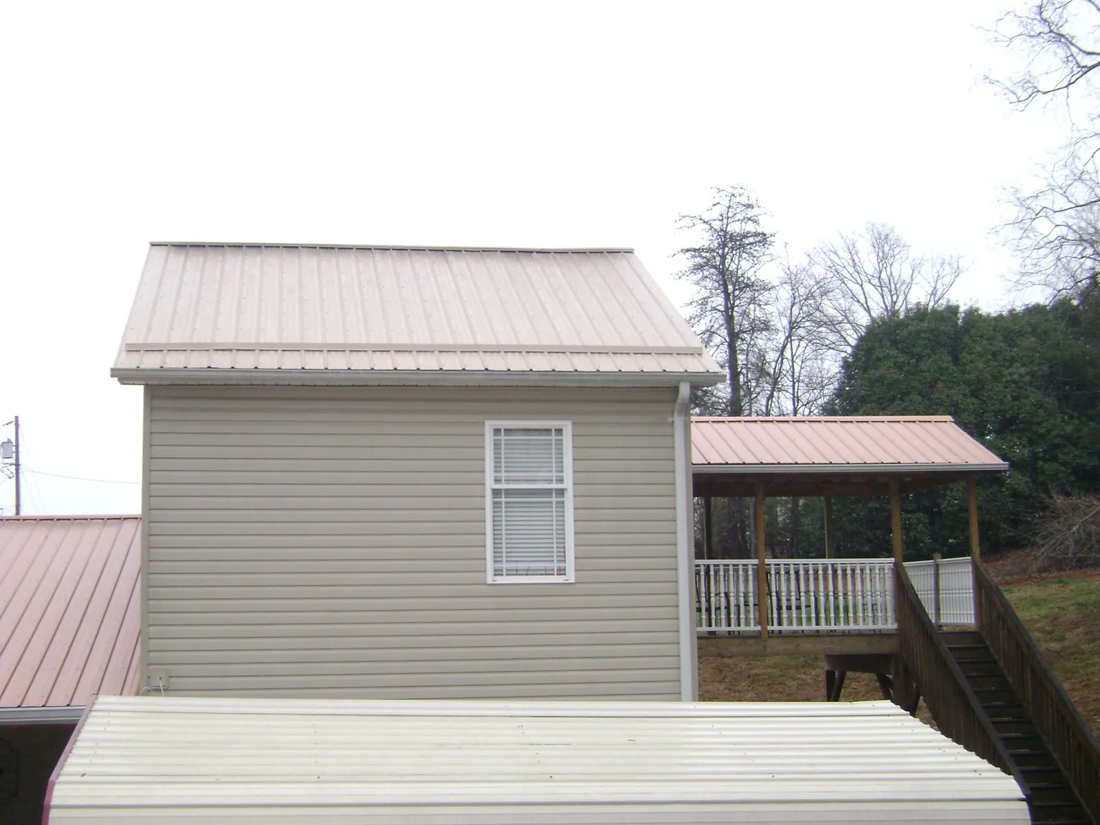 Tan metal roofs on a two story addition and attached porch, from a Roof Replacement job in Orrick